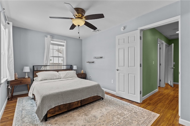 bedroom with a ceiling fan, baseboards, visible vents, and wood finished floors