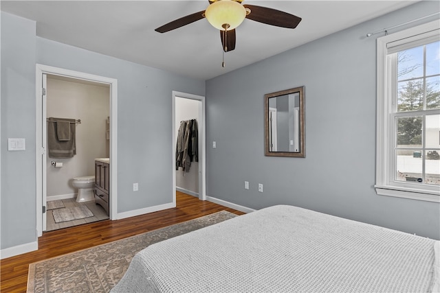 bedroom with dark wood-style flooring, a closet, a spacious closet, ensuite bath, and baseboards