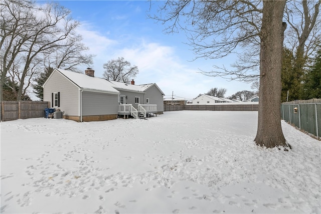 snow covered property featuring a fenced backyard, a chimney, and a wooden deck