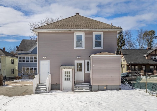 snow covered property featuring entry steps, roof with shingles, and fence