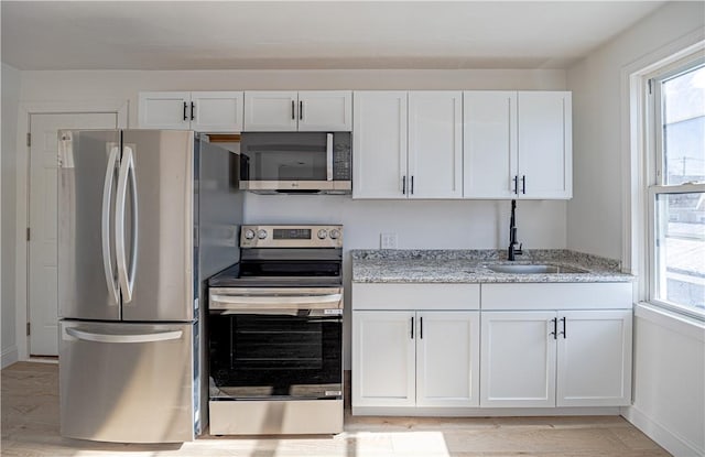 kitchen with stainless steel appliances, a sink, light stone countertops, and white cabinets