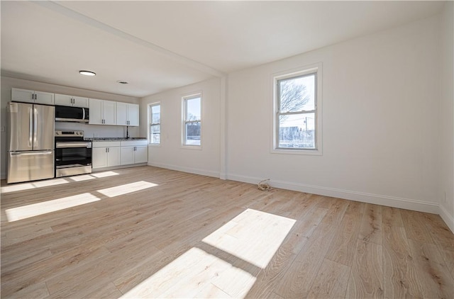 unfurnished living room with light wood-style flooring, baseboards, and a wealth of natural light