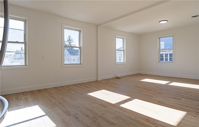 empty room with light wood-style floors, a wealth of natural light, and baseboards