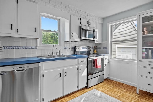 kitchen featuring white cabinets, dark countertops, glass insert cabinets, stainless steel appliances, and a sink