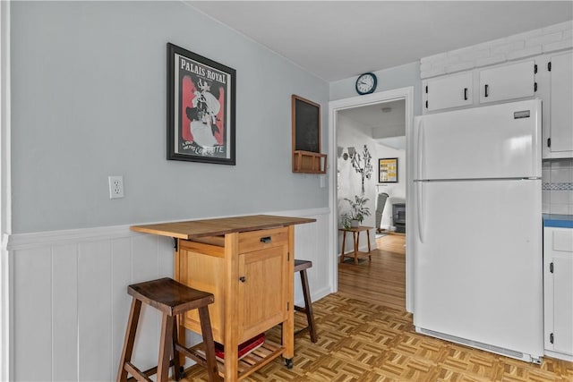 kitchen featuring white cabinets, a wainscoted wall, butcher block counters, a kitchen breakfast bar, and freestanding refrigerator