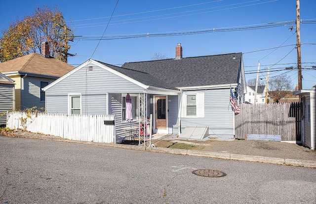 bungalow-style house featuring a chimney, fence, and roof with shingles