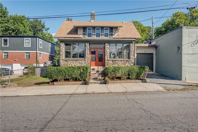 view of front of home featuring stone siding, fence, a chimney, and an attached garage