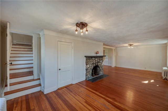 unfurnished living room with stairs, a stone fireplace, wood finished floors, and baseboards