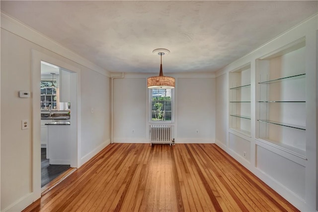 unfurnished dining area featuring radiator heating unit, built in features, light wood-style flooring, and baseboards