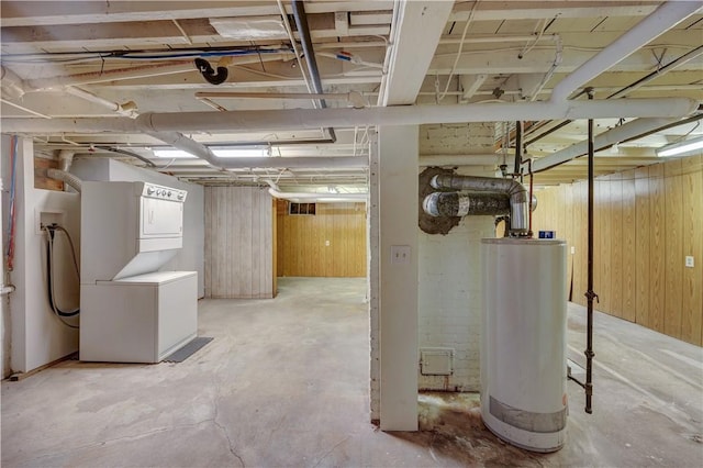 unfinished basement with stacked washer / dryer, gas water heater, and wood walls