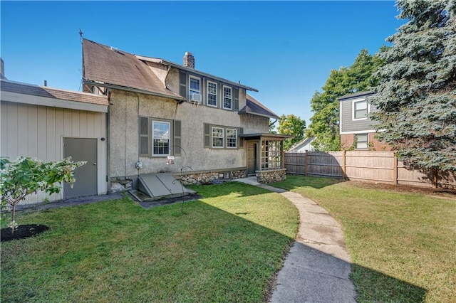 rear view of house featuring stucco siding, a lawn, a chimney, and fence