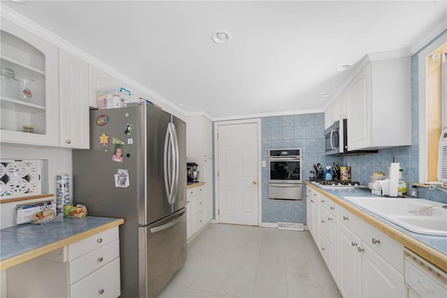 kitchen with white cabinets, glass insert cabinets, appliances with stainless steel finishes, crown molding, and a sink