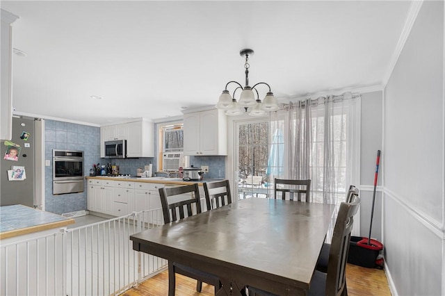 dining space with ornamental molding, light wood-type flooring, and a notable chandelier