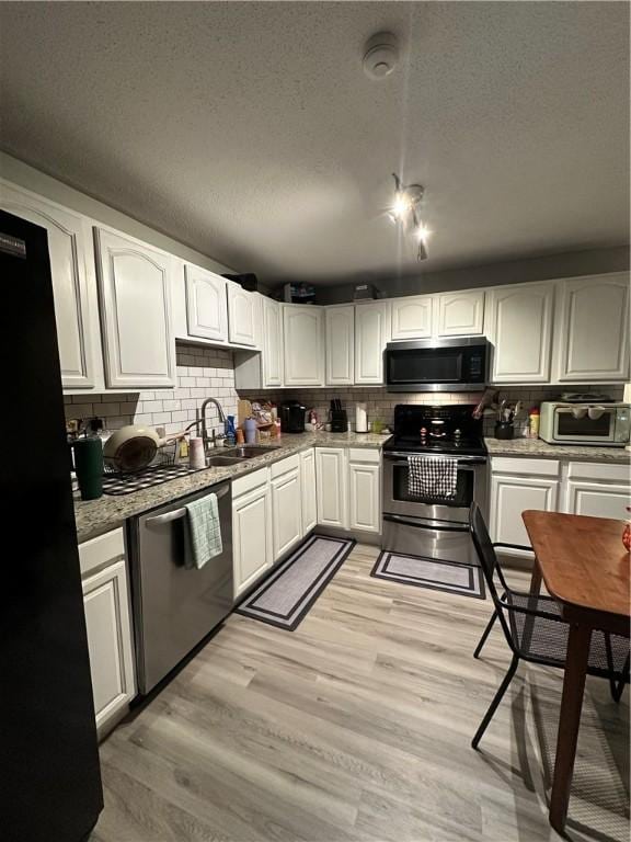 kitchen featuring stainless steel appliances, backsplash, light wood-style flooring, and white cabinets