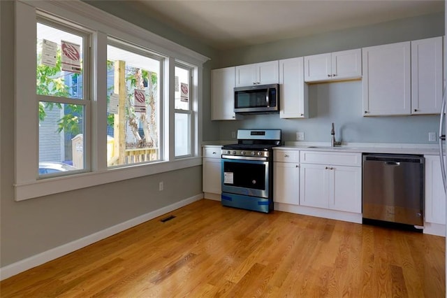 kitchen with light wood finished floors, white cabinets, stainless steel appliances, light countertops, and a sink