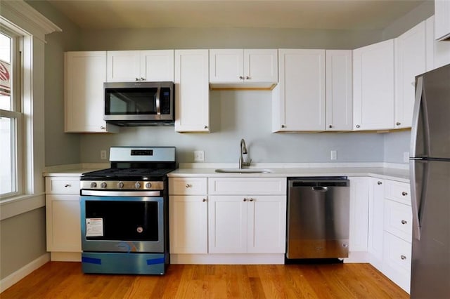 kitchen with stainless steel appliances, a sink, white cabinets, light countertops, and light wood-type flooring