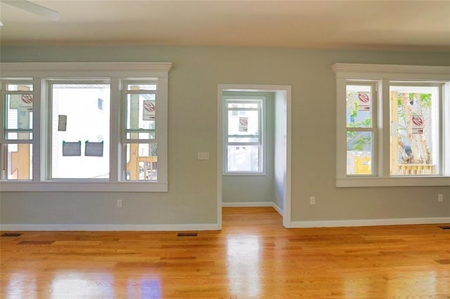 unfurnished room featuring visible vents, light wood-type flooring, a wealth of natural light, and baseboards