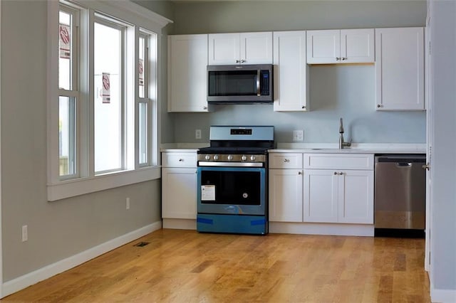 kitchen with white cabinets, light wood-style flooring, stainless steel appliances, light countertops, and a sink