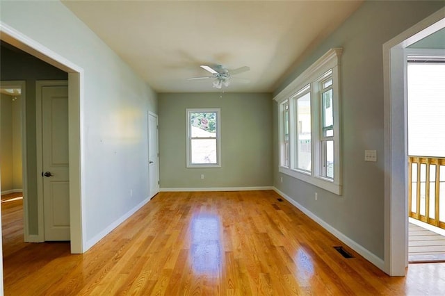 empty room featuring light wood-style floors, visible vents, baseboards, and a ceiling fan