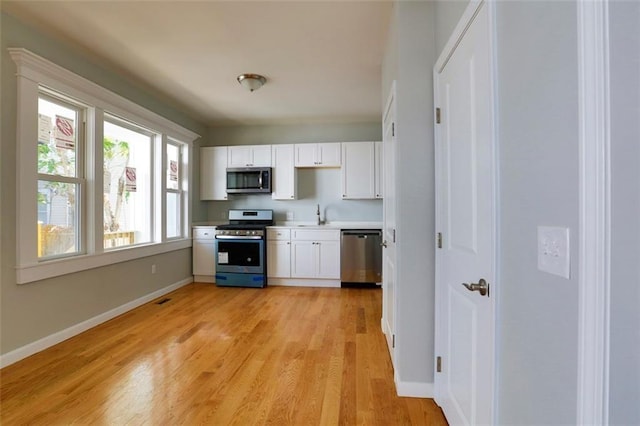 kitchen with baseboards, light wood-style floors, light countertops, appliances with stainless steel finishes, and white cabinets