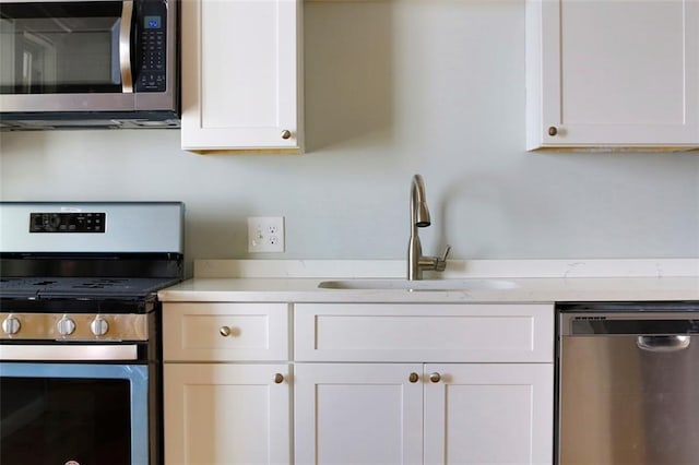 kitchen with light countertops, appliances with stainless steel finishes, a sink, and white cabinetry