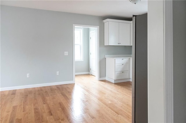 kitchen with light countertops, light wood-style floors, white cabinetry, and baseboards