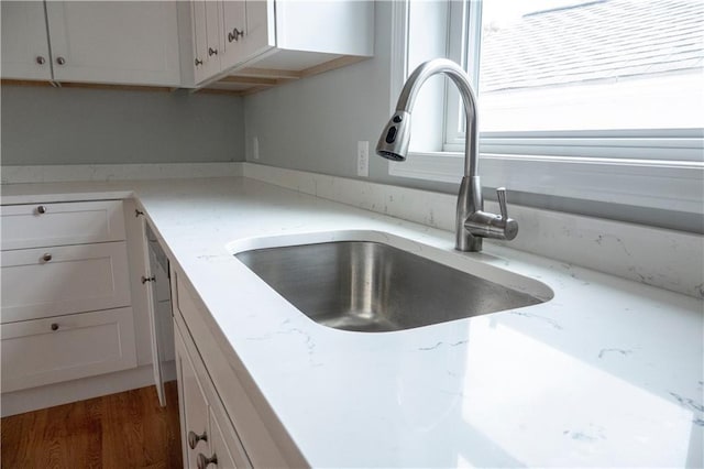 details featuring white cabinetry, light stone counters, a sink, and wood finished floors