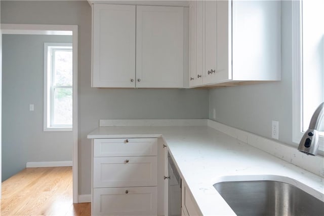 kitchen featuring light stone counters, stainless steel dishwasher, light wood-style floors, white cabinetry, and a sink