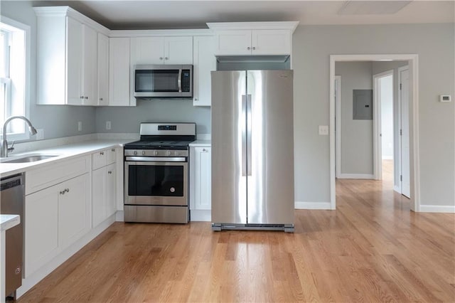 kitchen with stainless steel appliances, light countertops, white cabinets, a sink, and light wood-type flooring