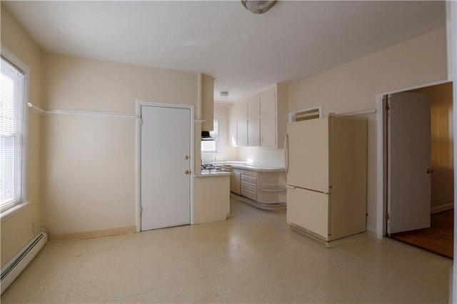 kitchen with light floors, light countertops, a baseboard heating unit, freestanding refrigerator, and plenty of natural light