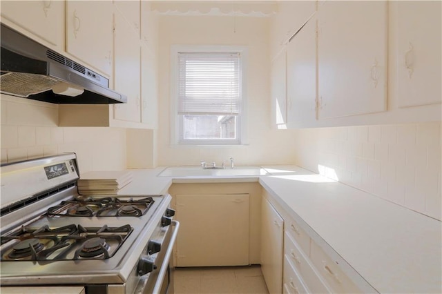 kitchen featuring decorative backsplash, range with gas stovetop, light countertops, under cabinet range hood, and light tile patterned flooring