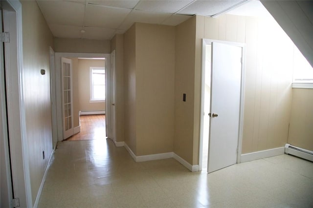 corridor with a baseboard heating unit, light floors, a paneled ceiling, and baseboards