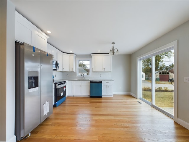 kitchen featuring appliances with stainless steel finishes, white cabinets, a sink, and pendant lighting