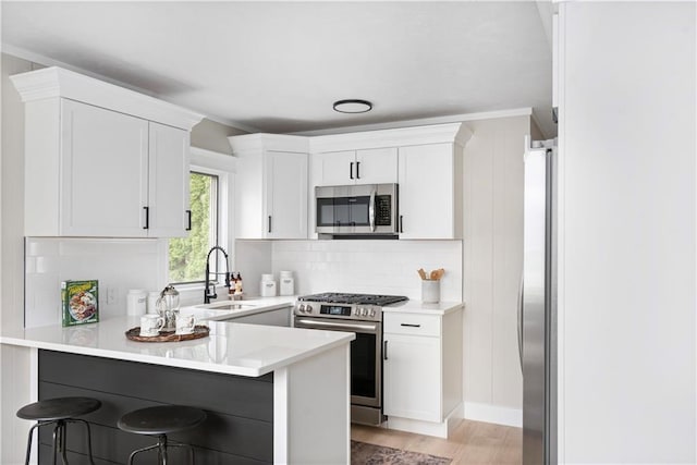 kitchen featuring white cabinets, a kitchen breakfast bar, light countertops, stainless steel appliances, and a sink