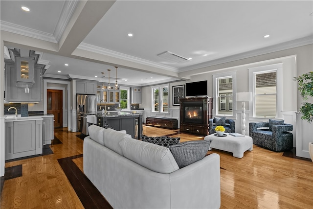 living area featuring light wood-type flooring, recessed lighting, ornamental molding, and a glass covered fireplace