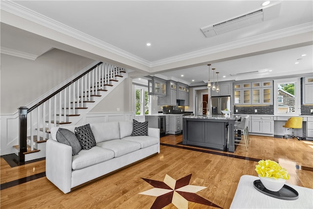 living area with light wood-style flooring, crown molding, a decorative wall, and stairway