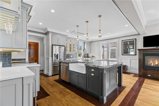 kitchen with a center island with sink, decorative light fixtures, stainless steel appliances, gray cabinets, and a sink