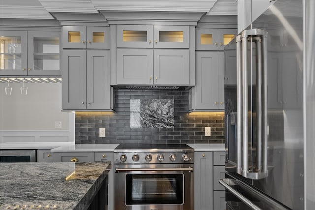 kitchen with premium appliances, gray cabinetry, decorative backsplash, and dark stone countertops