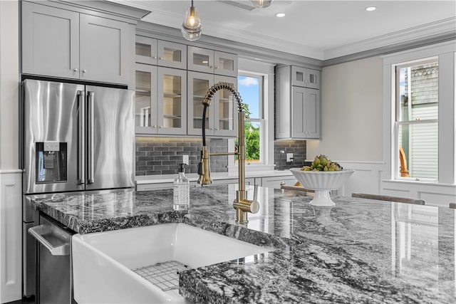 kitchen featuring a sink, dark stone countertops, stainless steel fridge, glass insert cabinets, and crown molding