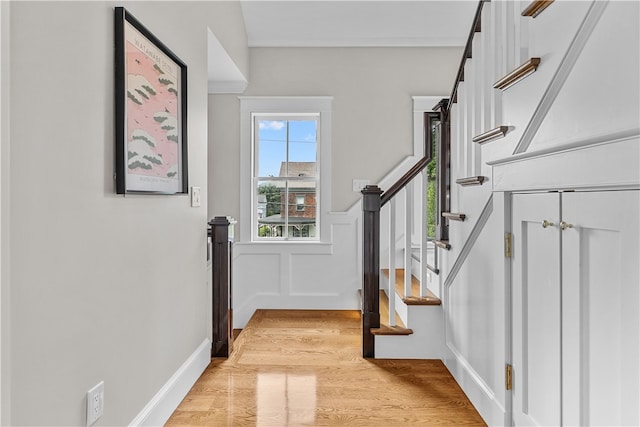 entrance foyer with light wood finished floors, stairway, wainscoting, and a decorative wall