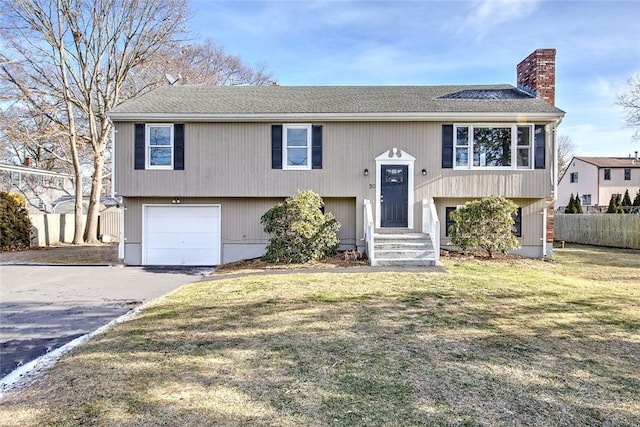 bi-level home with a garage, a chimney, aphalt driveway, fence, and a front yard