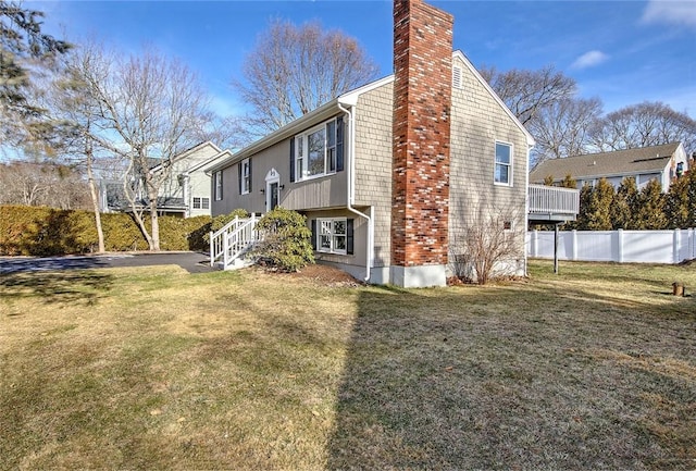 view of property exterior featuring fence, a chimney, and a lawn