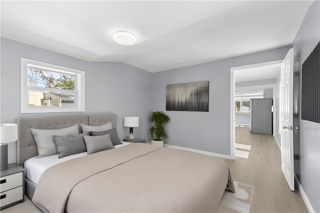 bedroom featuring lofted ceiling, light wood-style flooring, freestanding refrigerator, and baseboards