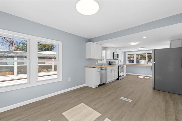 kitchen featuring baseboards, white cabinets, wood counters, appliances with stainless steel finishes, and a sink