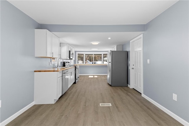 kitchen with stainless steel appliances, visible vents, wooden counters, white cabinets, and baseboards