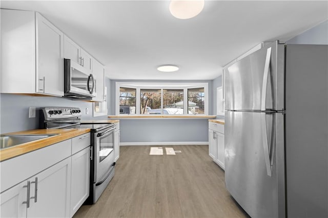 kitchen with light wood finished floors, stainless steel appliances, light countertops, white cabinetry, and baseboards