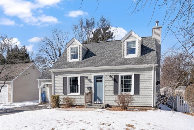 cape cod-style house featuring a shingled roof and a chimney