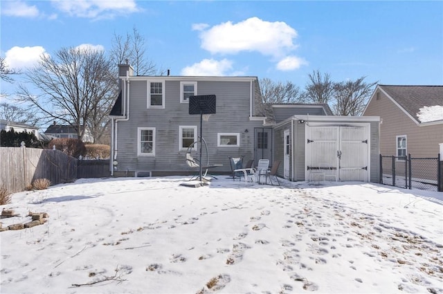 snow covered house featuring entry steps, fence, an outbuilding, and a storage unit