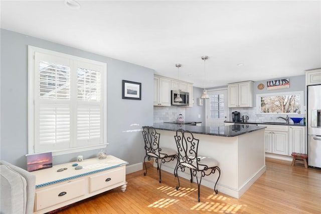 kitchen with stainless steel appliances, a peninsula, light wood-style floors, tasteful backsplash, and pendant lighting