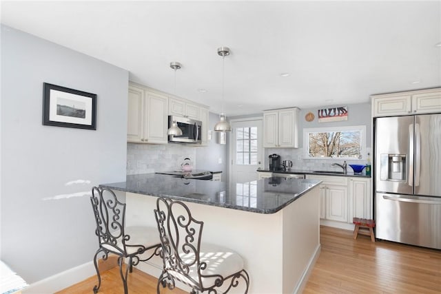 kitchen with pendant lighting, stainless steel appliances, light wood-style floors, dark stone countertops, and a peninsula